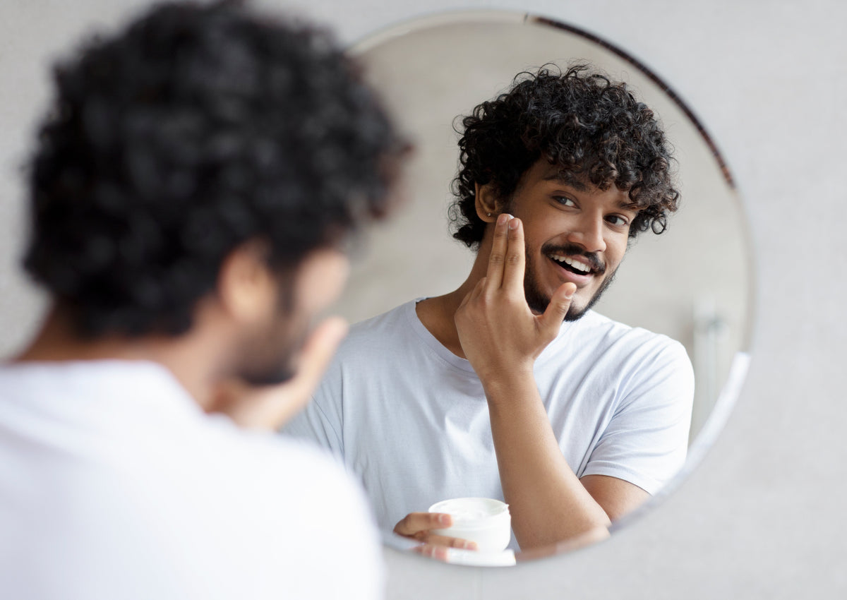Young Indian man applying moisturizer to his face