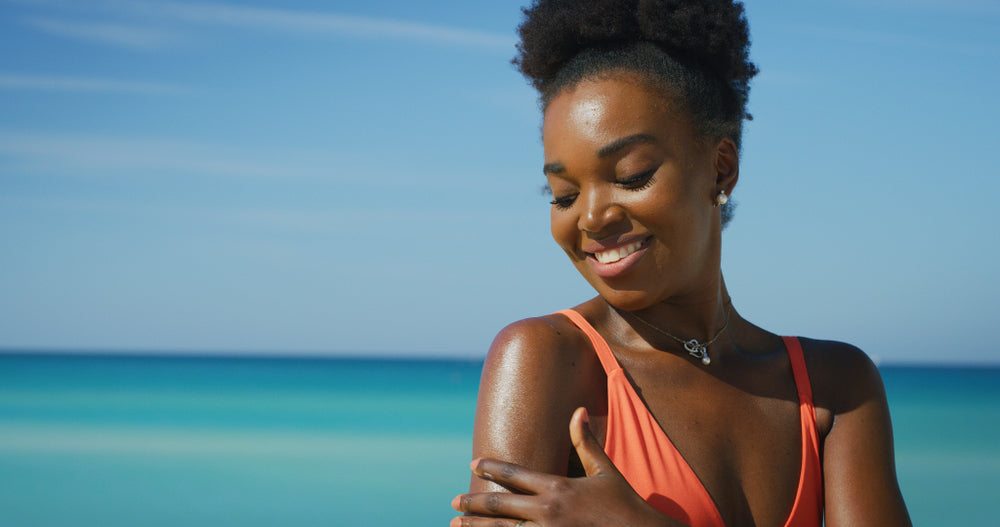 Woman at beach in swimsuit applying sunscreen to arm