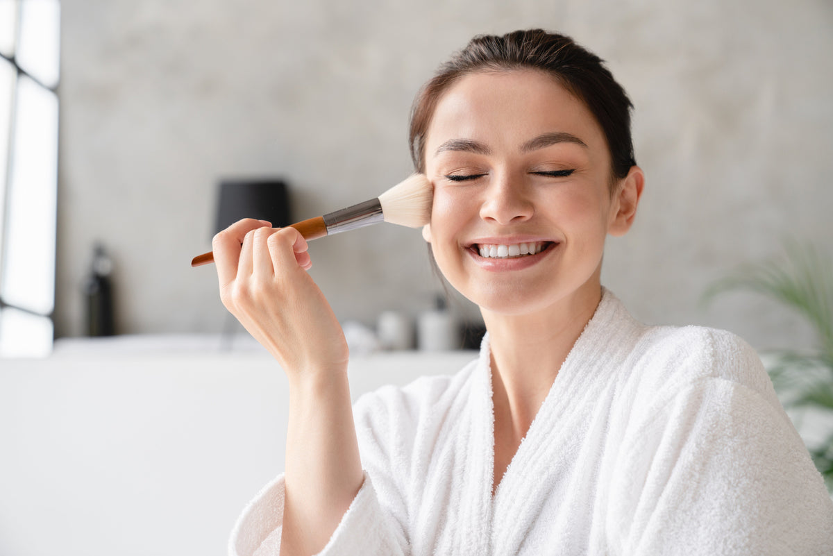 Happy woman applying hypoallergenic makeup to her face with a brush