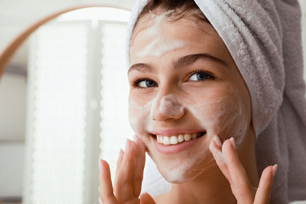 Teen girl smiling and scrubbing her face with cleanser.