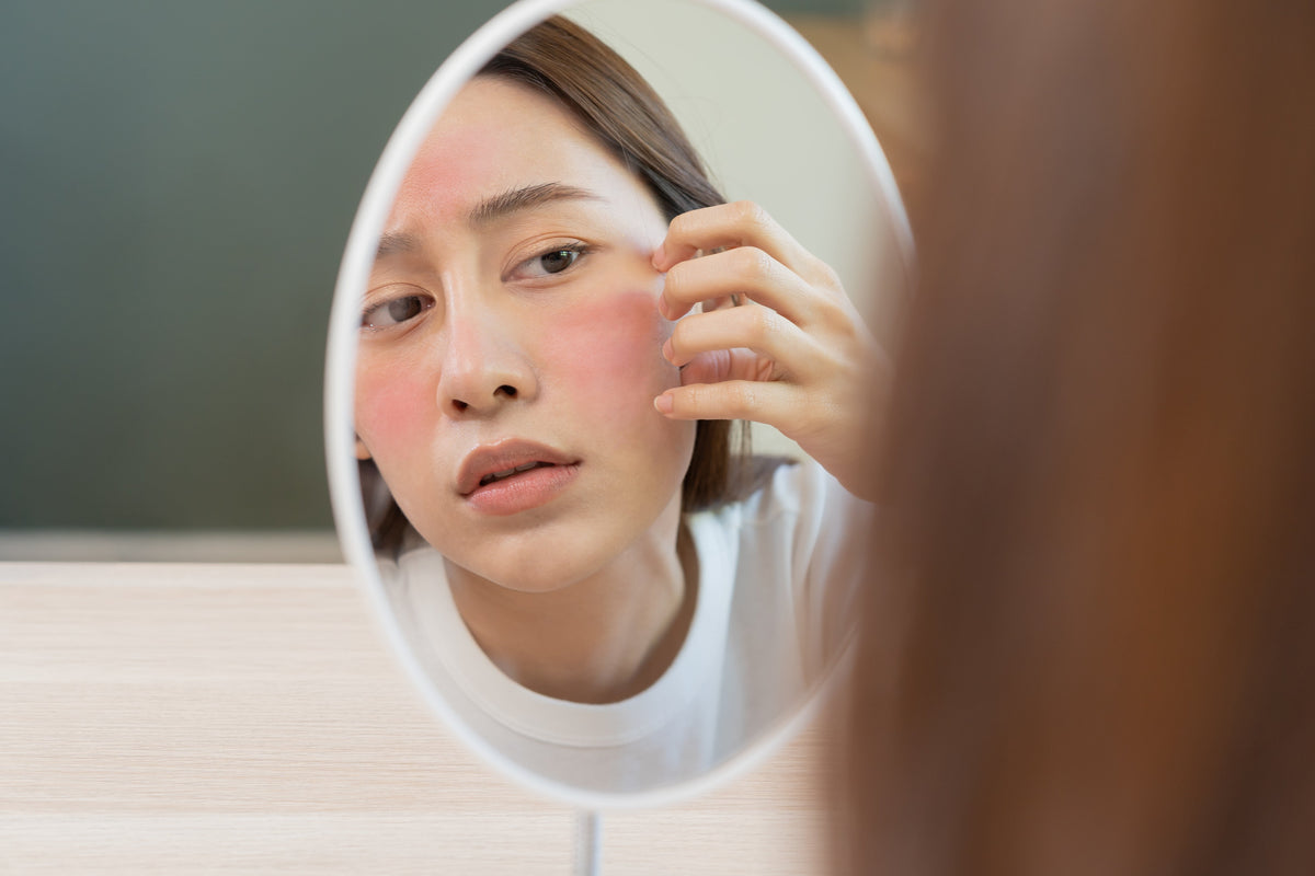 Woman looking in mirror at sensitive skin reaction on her face.