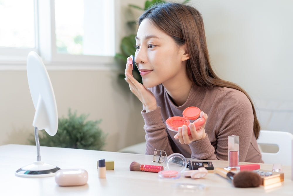 Young Asian woman applying makeup in front of a vanity.