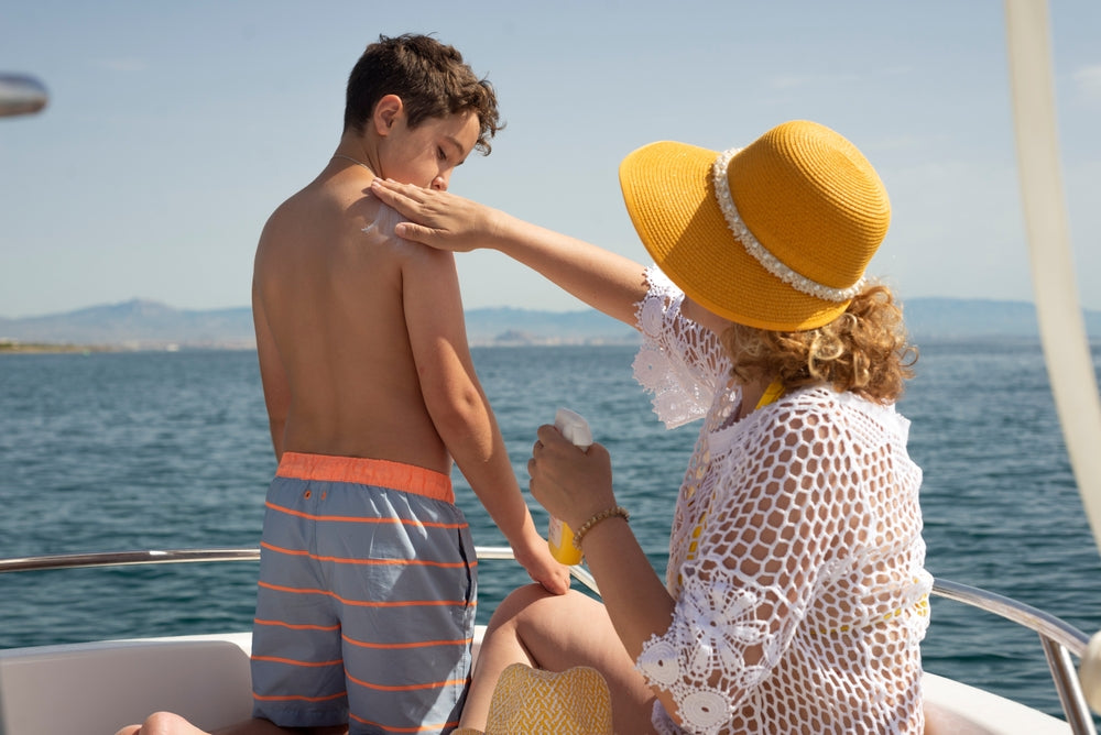 Mom putting sunscreen on young son while sitting on a boat