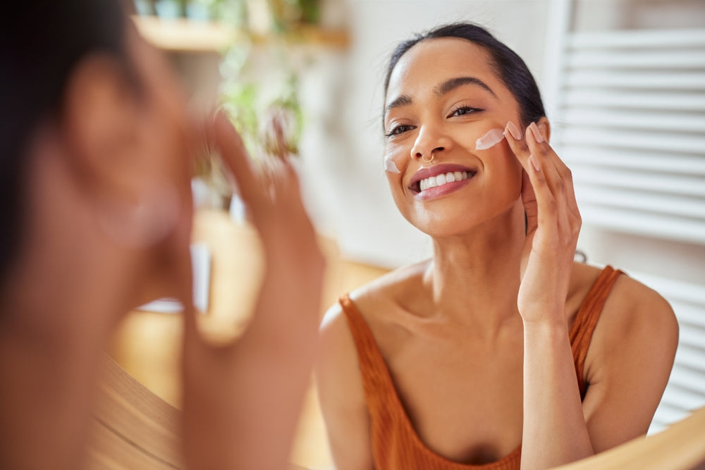 Woman staring at herself in the mirror while applying a face moisturizer