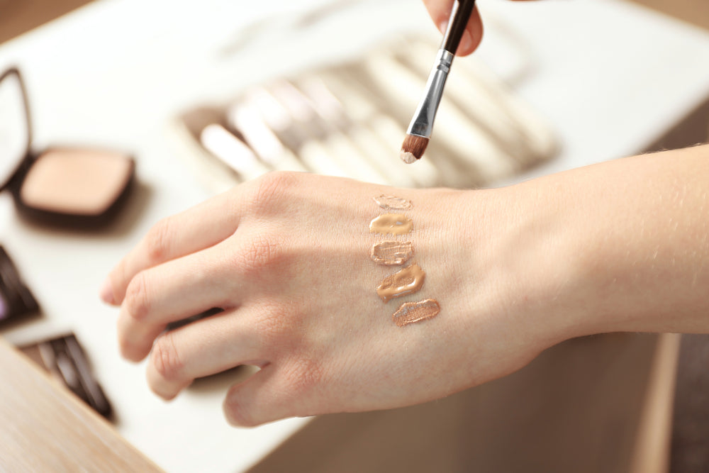 Close-up of a woman mixing different foundation colors on her hand.