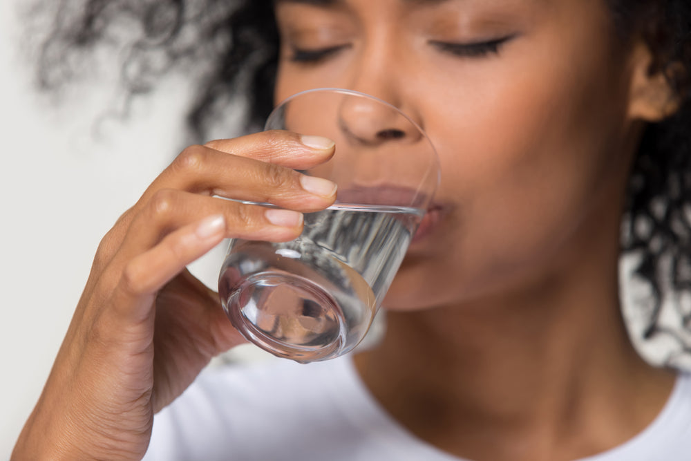 Image of young Black woman drinking a glass of water.