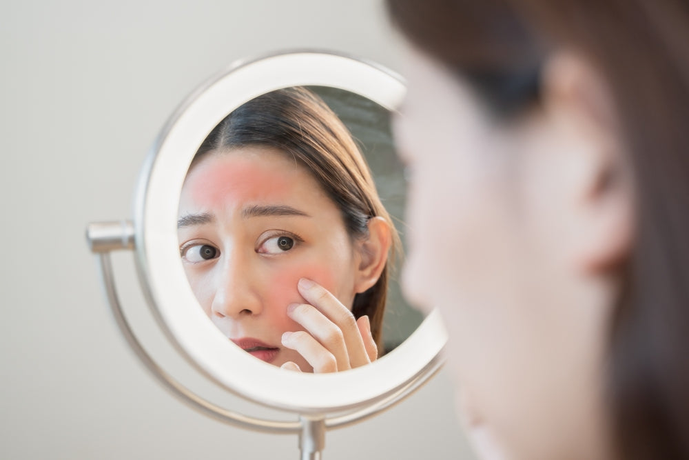 Woman looking at sunburn on her face in a mirror.