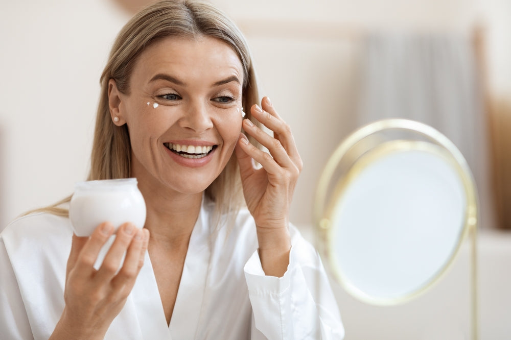 Image of woman applying an eye cream in front of a magnifying mirror.
