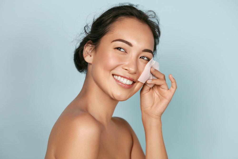 Image of a woman wiping an oil blotting sheet on her cheek.