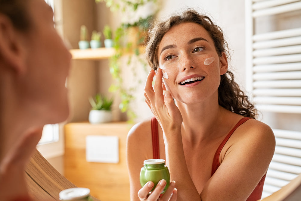 Image of woman in her bathroom applying skincare product to her cheeks.