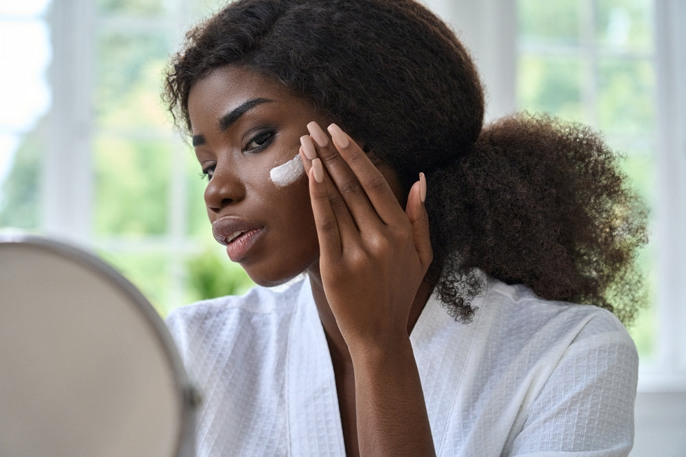 Young Black woman putting on moisturizer 