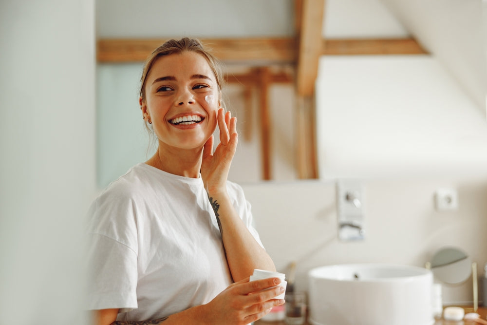 Young woman smiling while applying moisturizer to her cheek.