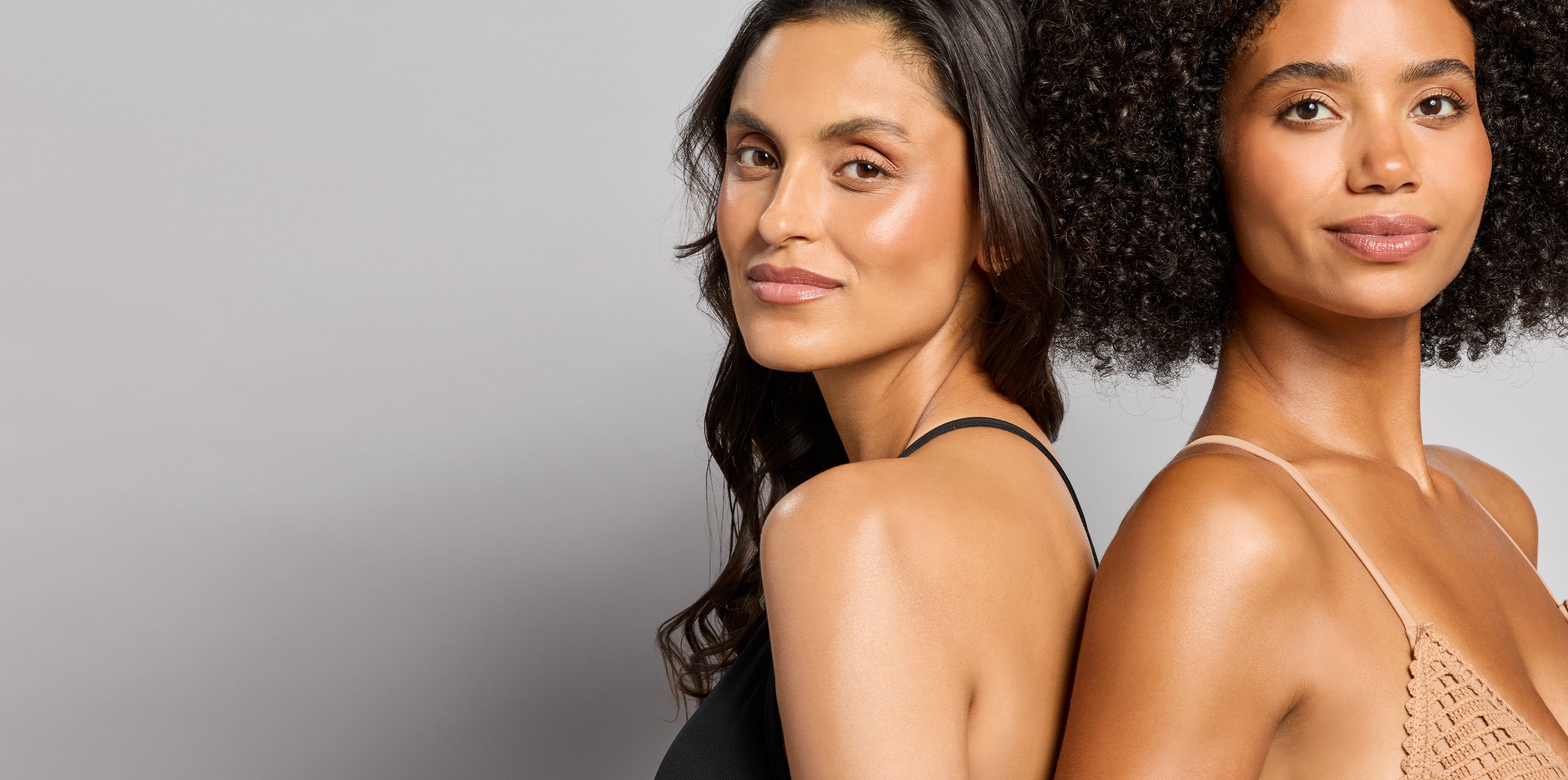 Two women standing back-to-back against a plain background wearing  total protection now -show body shield spf 50